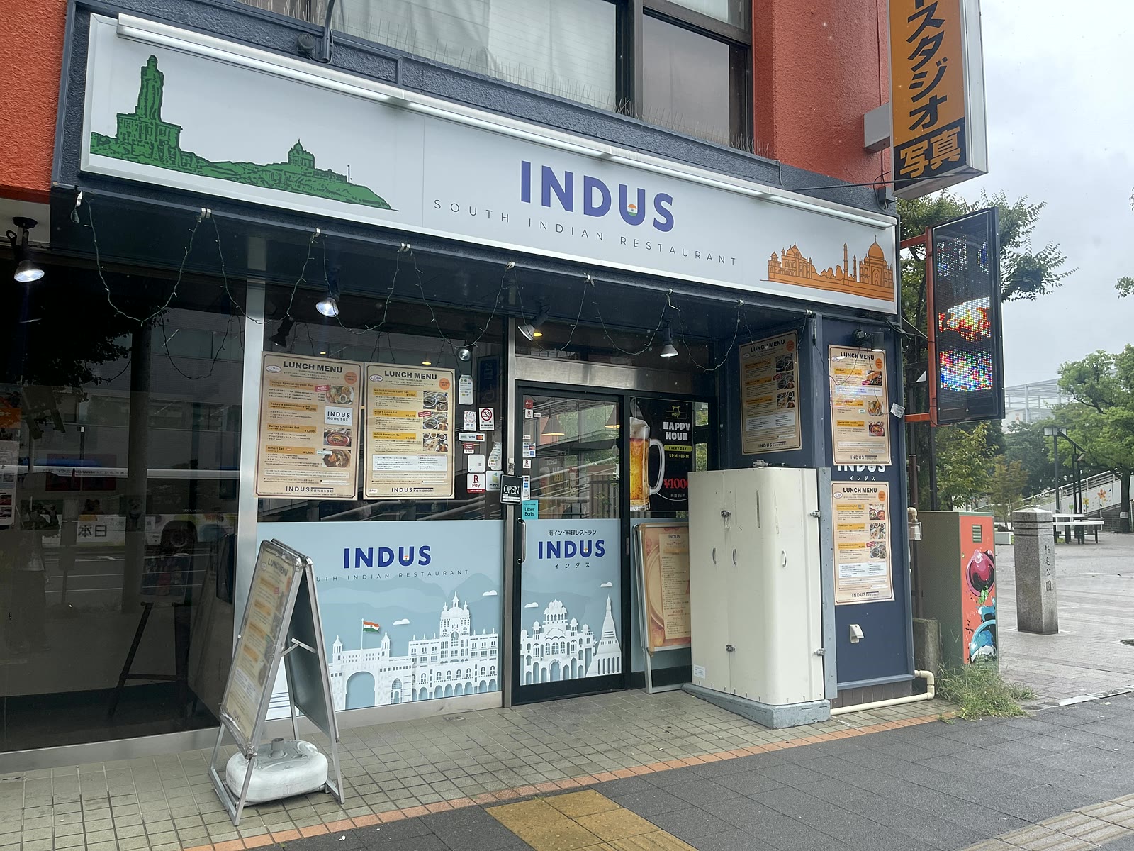 南インド料理レストランINDUS川崎の外観。白い看板に青字でINDUS SOUTH INDIAN RESTAURANTと書かれ、店先にランチメニューの写真が並ぶ