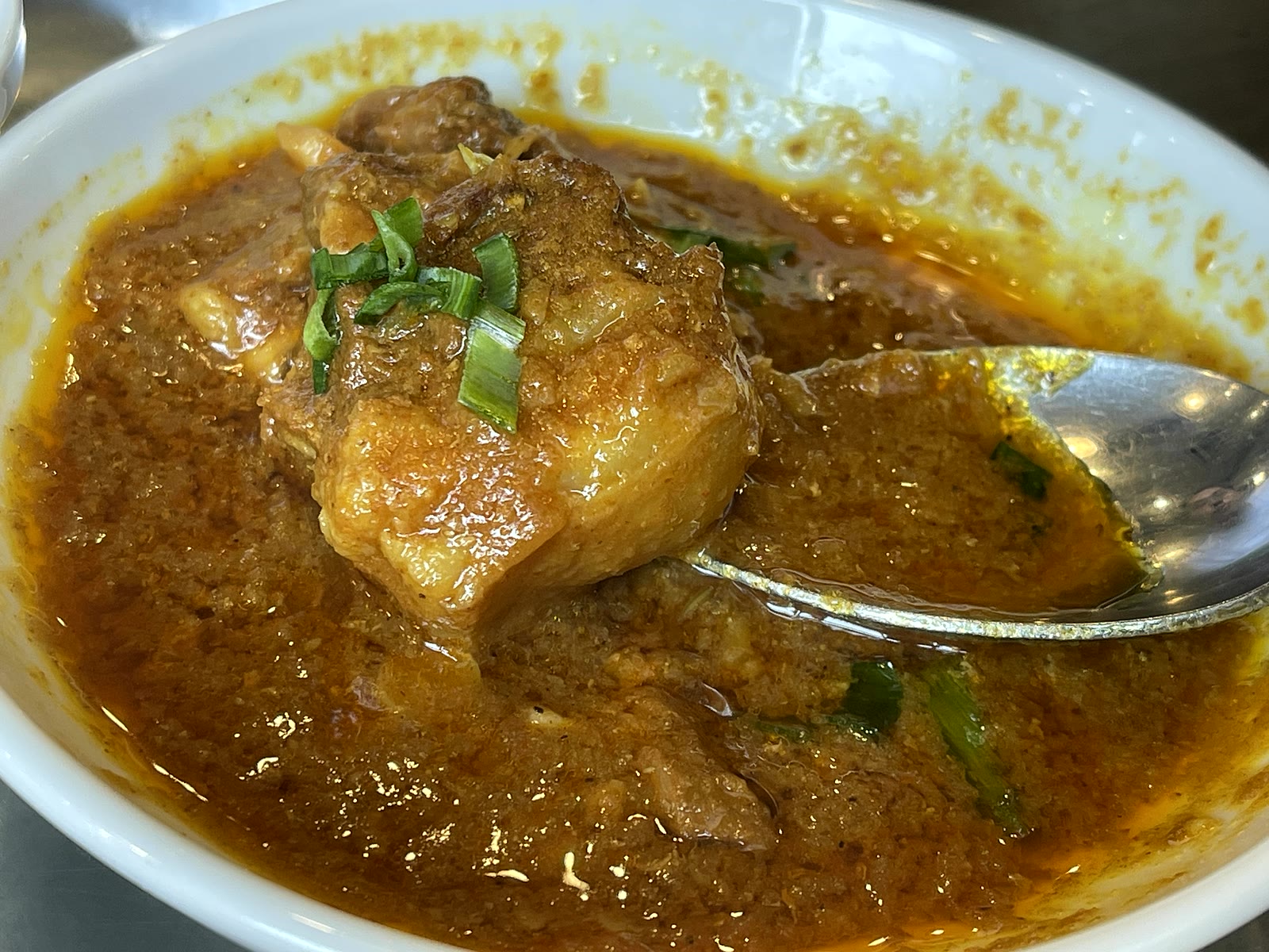 濃い茶色のラムカレーのアップ。ゴロッとしたラム肉の塊が入り、スプーンが添えられている