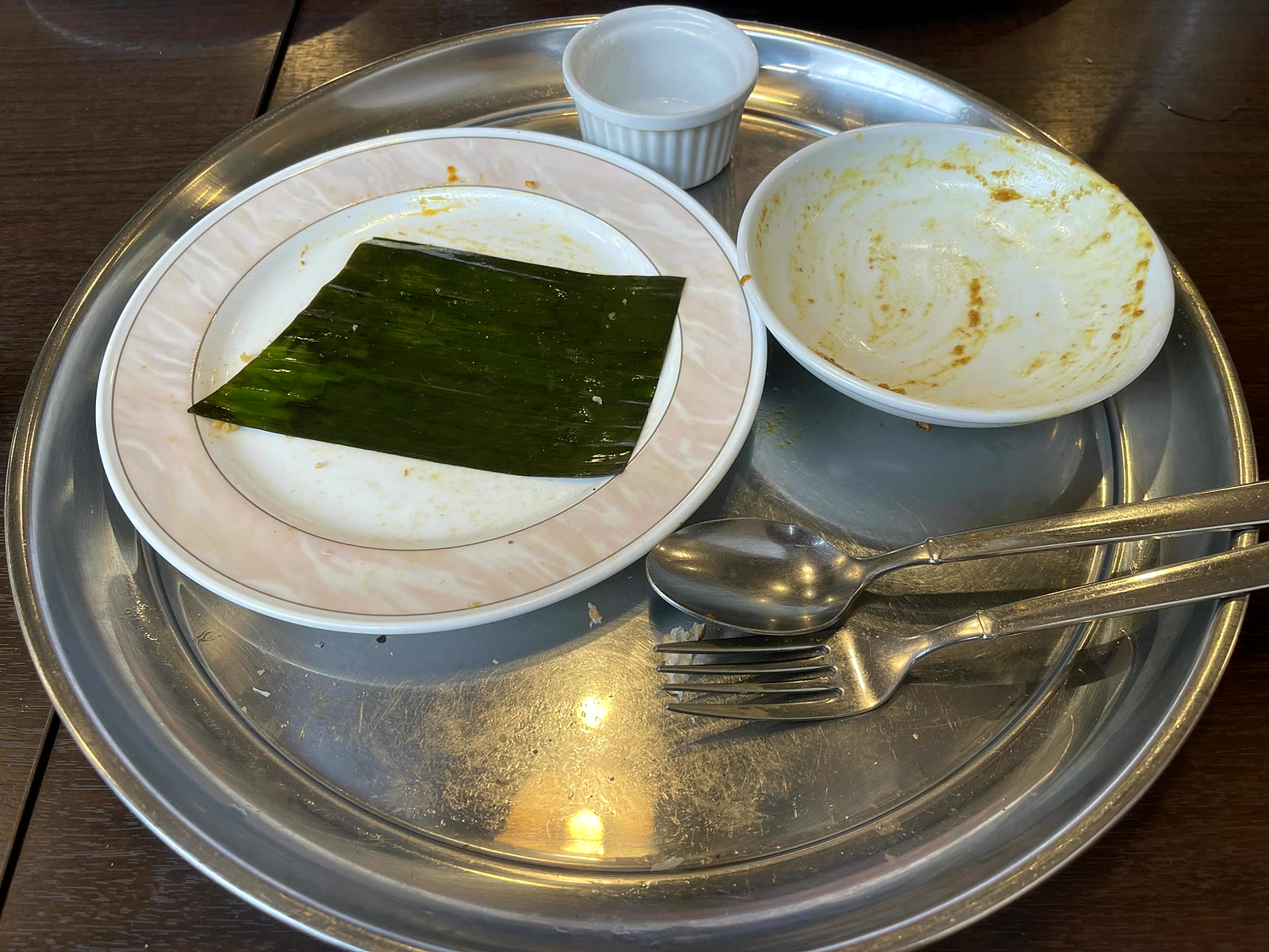 食べ終わったあとのトレイ。空になったカレーの器、バナナの葉だけが残ったビリヤニの皿、スプーンとフォークが置かれている