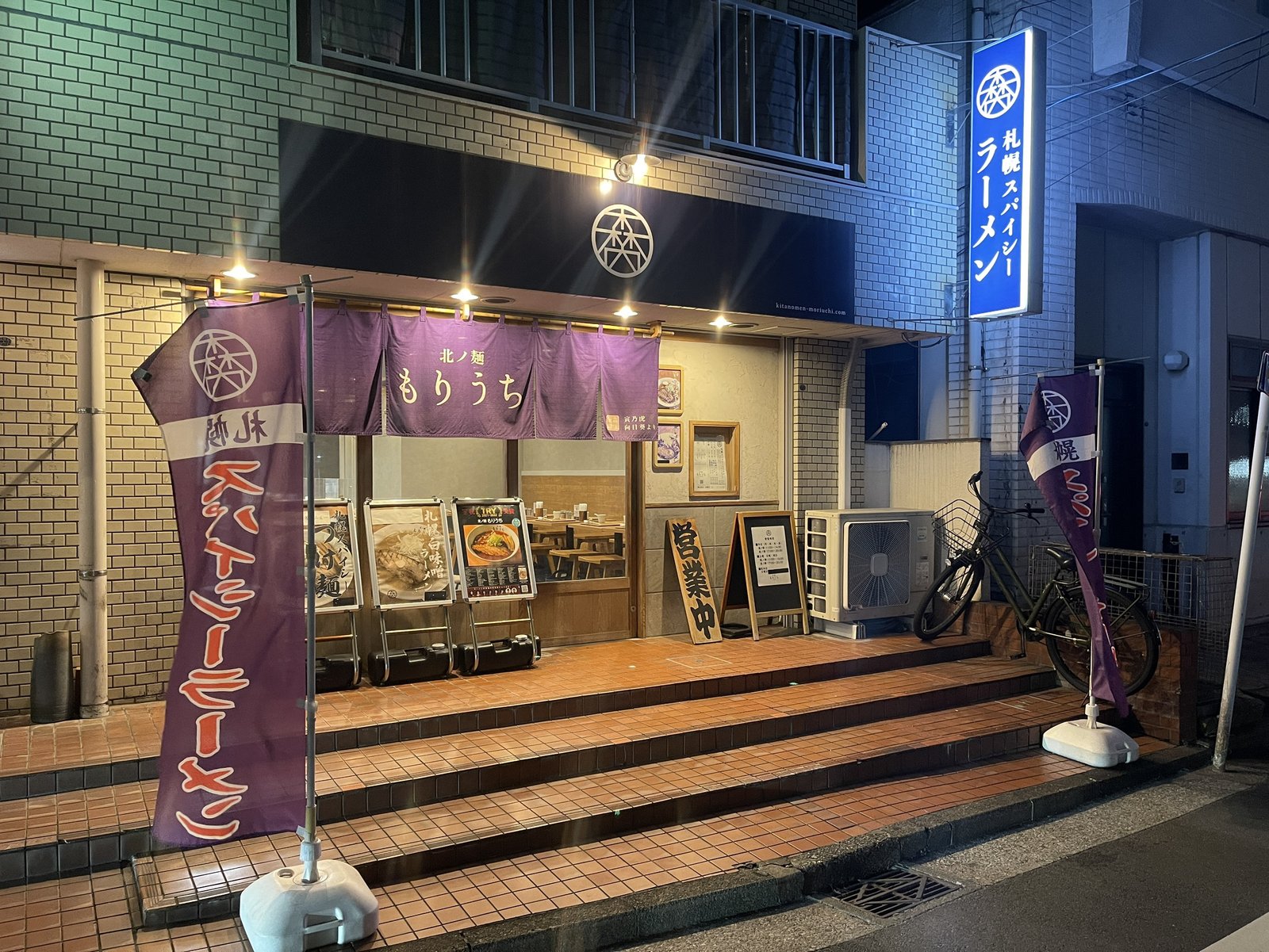 夜の「北ノ麺もりうち」店先、紫ののれんと「札幌スパイシーラーメン」の看板が目印