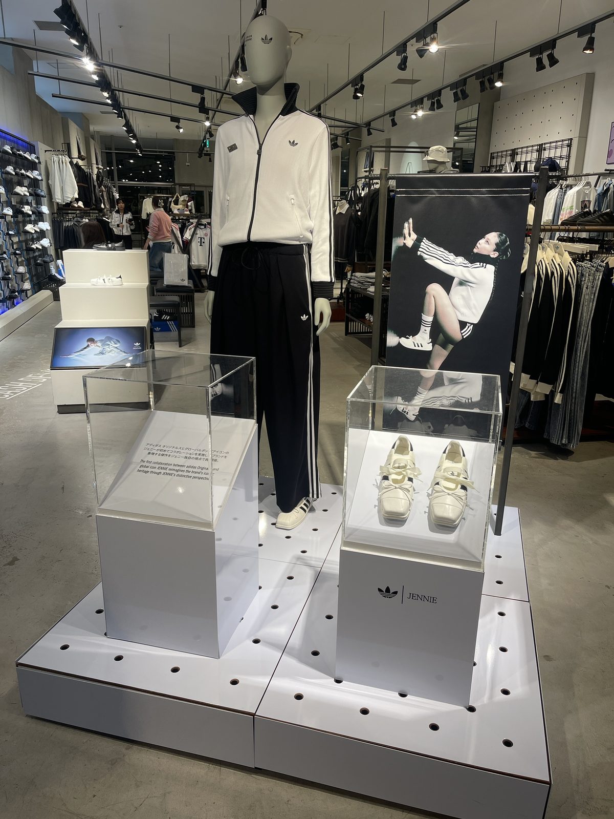 店内の adidas Originals by JENNIE 特設ディスプレイ。白のトラックトップと黒のトラックパンツを着たマネキンとキャンペーンビジュアル