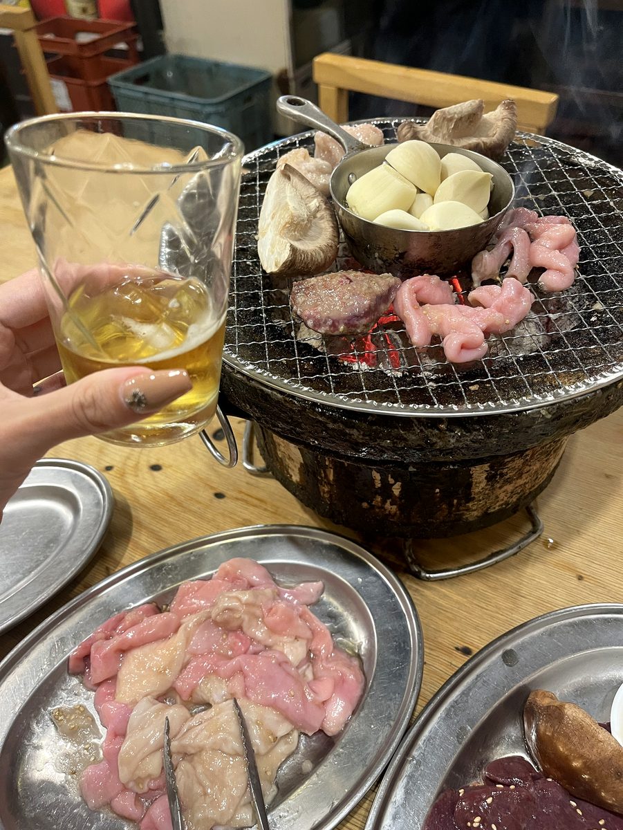 七輪でしいたけやにんにく、ホルモンを焼きながら瓶ビールで乾杯する様子
